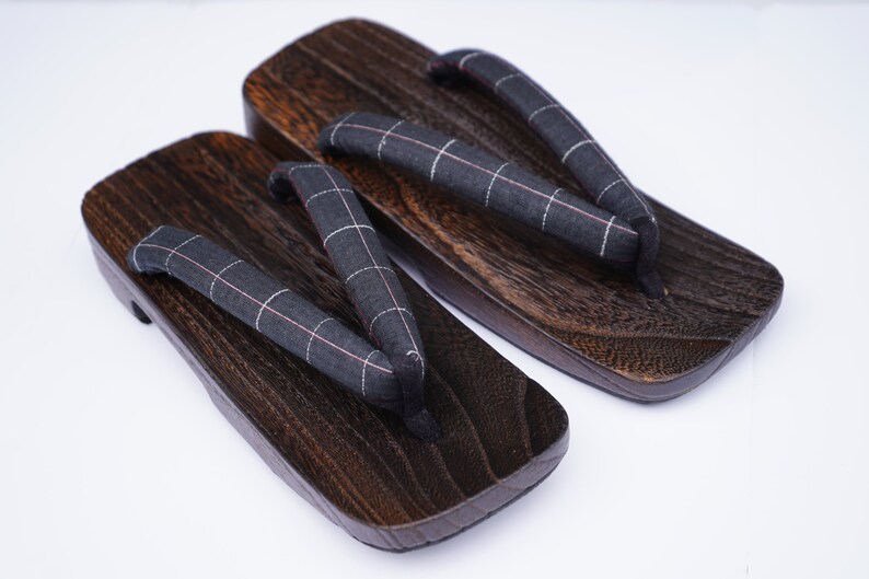May include: A pair of dark brown wooden geta sandals with black and white checkered fabric straps.