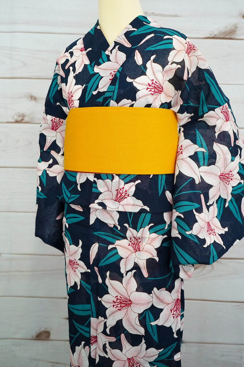 Puede incluir: Un yukata azul marino con un estampado floral de lirios blancos y un obi amarillo. El yukata es una prenda tradicional japonesa que se usa durante los meses de verano.