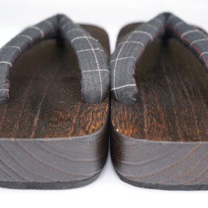 May include: A pair of dark brown wooden geta sandals with black and white checkered fabric straps.