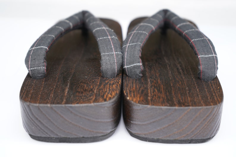 May include: A pair of dark brown wooden geta sandals with black and white checkered fabric straps.