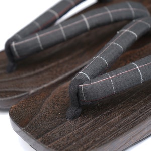 May include: A pair of dark brown wooden geta sandals with black and white checkered fabric straps.