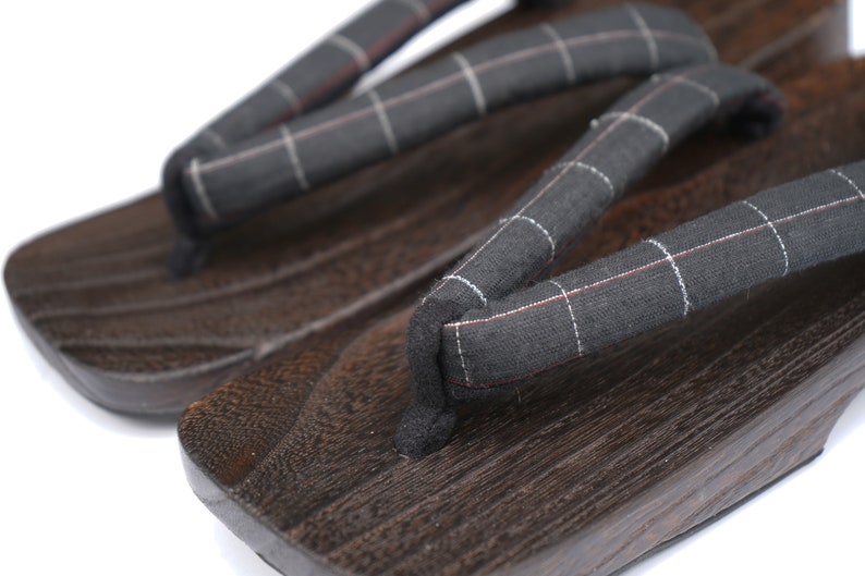 May include: A pair of dark brown wooden geta sandals with black and white checkered fabric straps.
