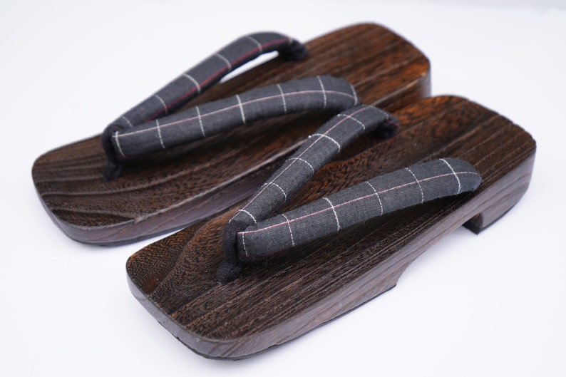 May include: A pair of dark brown wooden geta sandals with black and white checkered fabric straps.