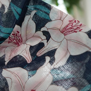 Puede incluir: Primer plano de una tela azul oscuro con un patr&oacute;n floral blanco y rosa. La tela tiene una superficie texturizada y las flores son lirios.