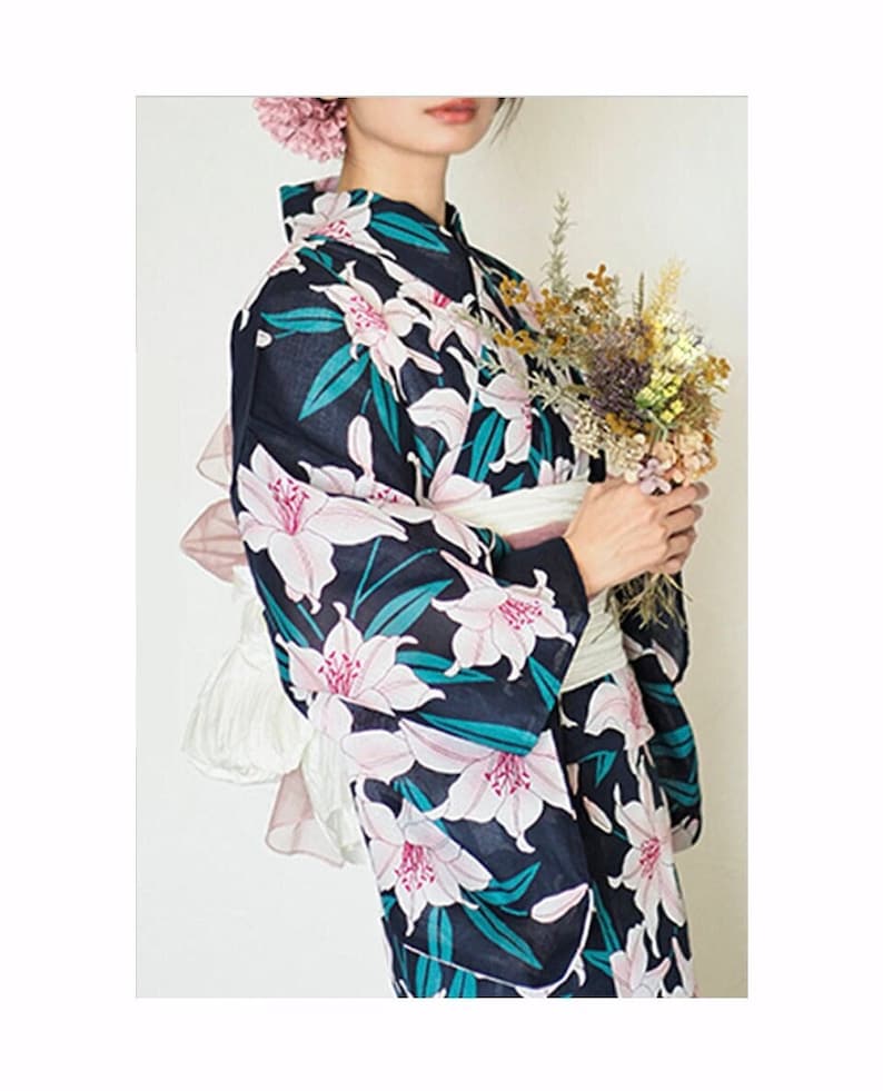 Puede incluir: Un yukata azul marino con un estampado floral blanco y rosa. El yukata tiene una faja blanca y lo lleva puesto una persona que sostiene un ramo de flores secas.