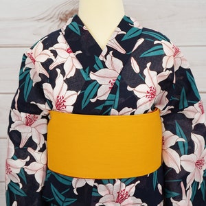 Puede incluir: Un yukata azul marino con un estampado floral de lirios blancos y una faja obi amarilla.