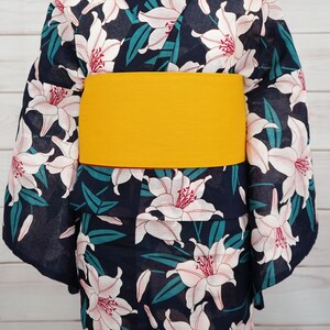 Puede incluir: Un yukata azul marino con un estampado floral de lirios blancos y una faja amarilla. El yukata es una prenda tradicional japonesa que se usa durante los meses de verano.