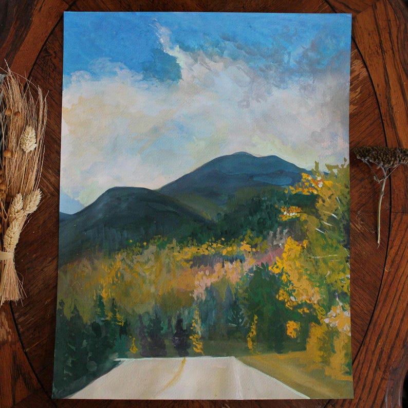 May include: An original landscape painting depicts a mountain scene with a road leading into the distance. The sky is blue with white clouds. The foreground features a road, and the sides of the road are lined with trees in shades of green and yellow.