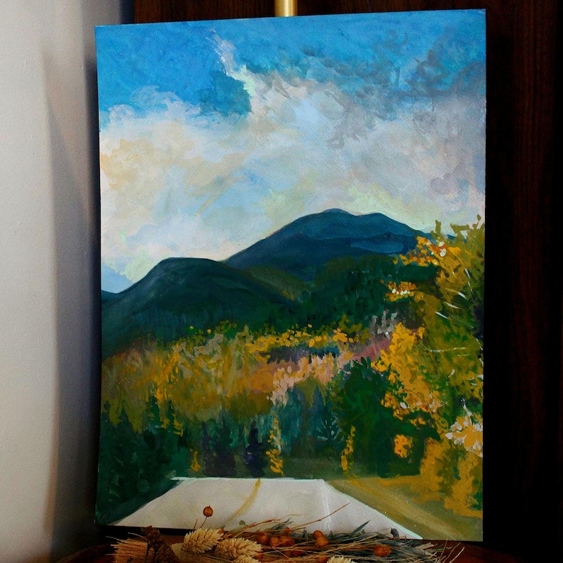 May include: An acrylic painting of a mountain landscape. The artwork features a road leading towards dark green mountains under a blue sky with white and gray clouds. Yellow and green trees line the road.