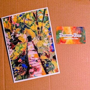 May include: A rectangular art print featuring an impressionistic painting of a path surrounded by vibrant yellow, green, pink, and blue foliage. Beside it is a small rectangular business card with the text Jasmine Rose multimedia fine artist.