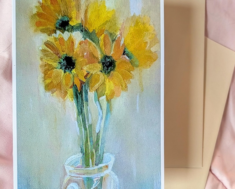 Puede incluir: Pintura a la acuarela de girasoles en un jarr&oacute;n de cristal. Los girasoles son amarillos con centros oscuros y tallos verdes. El jarr&oacute;n es transparente y el fondo es de un color suave y neutro. Un sobre beige est&aacute; al lado de la pintura.