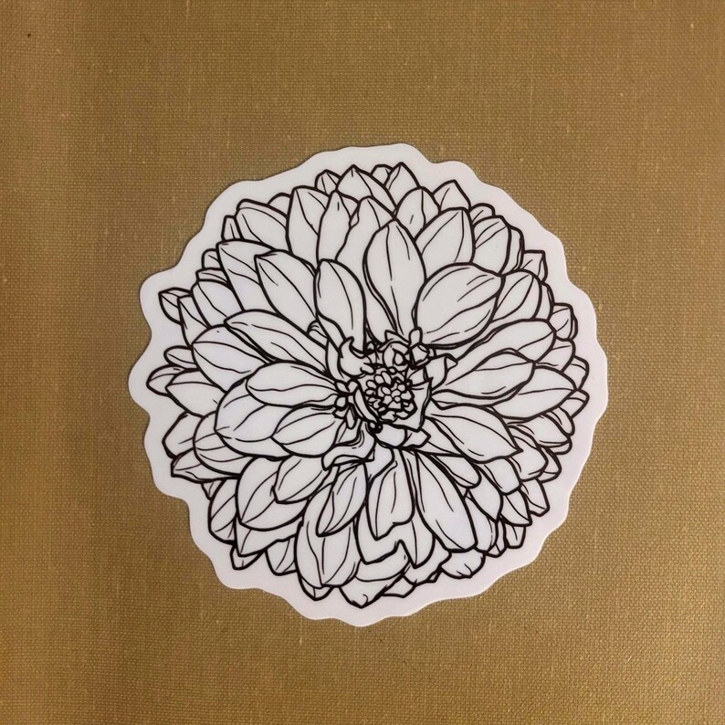 May include: A white sticker featuring a detailed black line drawing of a dahlia flower. The flower has numerous petals arranged in layers, with a textured appearance. The sticker is on a tan background.