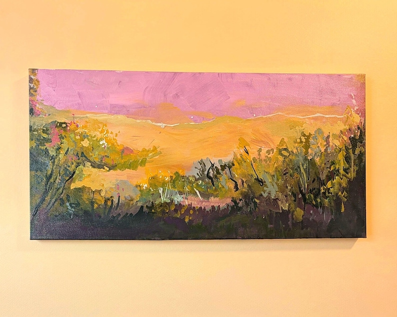May include: An original landscape painting on canvas. The artwork depicts a vibrant sunset with a pink sky and a golden horizon. The foreground features lush green and yellow foliage, with dark purple shadows at the base. The painting is rectangular and mounted on a wall.