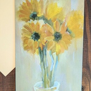 Puede incluir: Una pintura de acuarela de girasoles en un jarr&oacute;n de cristal. Los girasoles son amarillos con centros oscuros, y el jarr&oacute;n es transparente. El fondo es de un color suave y apagado. La pintura est&aacute; en una tarjeta de felicitaci&oacute;n.