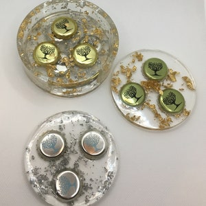 Puede incluir: Conjunto de tres posavasos redondos con base de resina transparente y purpurina dorada o plateada. Cada posavasos presenta tres tapas de botella con un diseño de árbol.