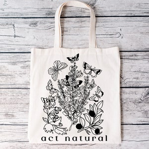 May include: A white tote bag with black line art of flowers, leaves, and butterflies. The text "act natural" is printed at the bottom of the bag.