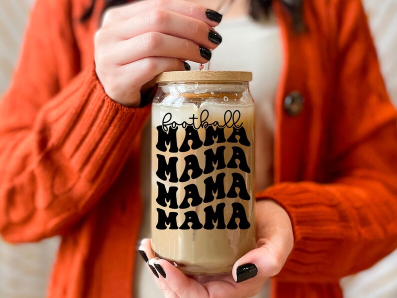 May include: A clear glass jar with a wooden lid and a black and white graphic that says "football mama" repeated four times. The jar is filled with a light brown liquid.
