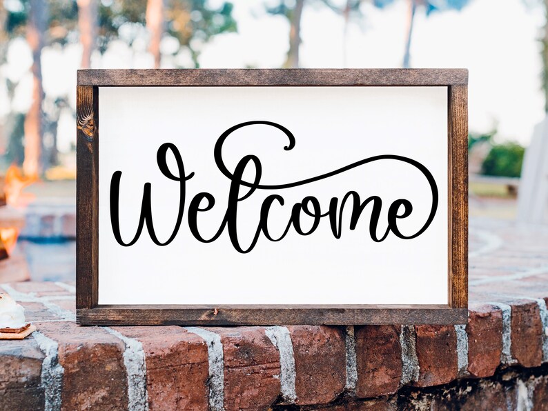 May include: A wooden framed sign with the word "Welcome" written in a decorative script font.