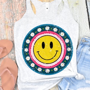 May include: A white tank top with a distressed, blue, pink, and white daisy print with a yellow smiley face in the center.