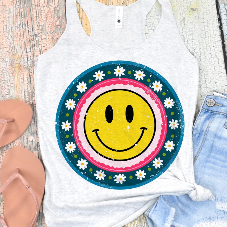 May include: A white tank top with a distressed, blue, pink, and white daisy print with a yellow smiley face in the center.