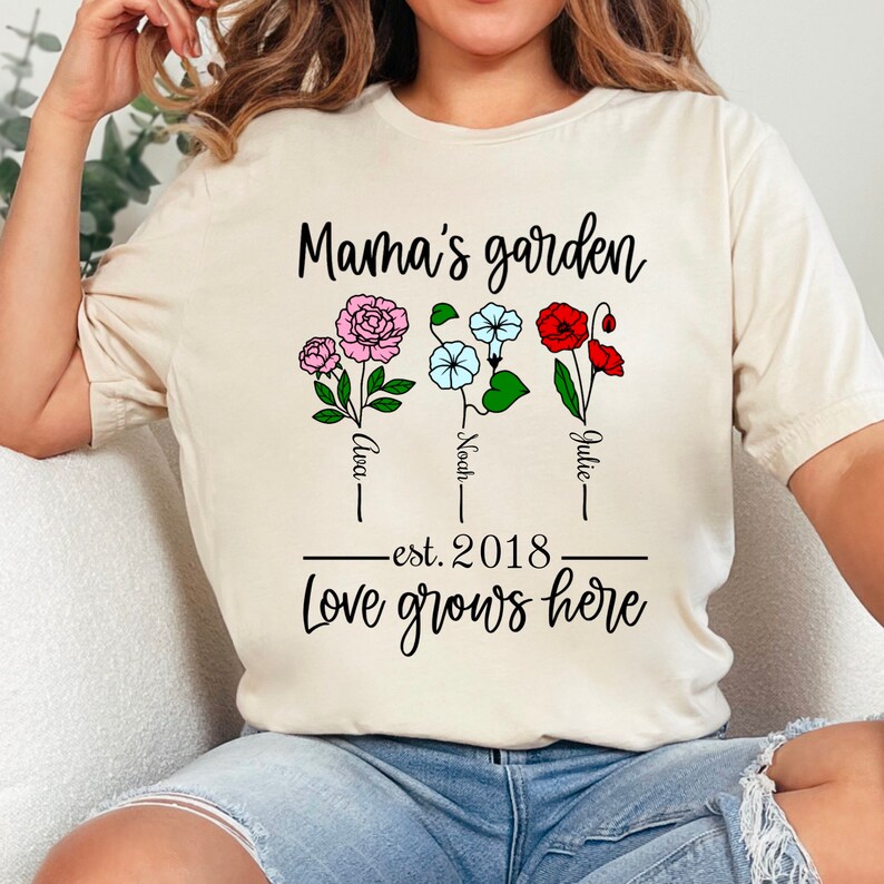 May include: A white t-shirt with the text "Mama's garden" and three flowers with the names "Ava", "Noah", and "Julie" below them. The text "est. 2018" and "Love grows here" are also printed on the shirt.