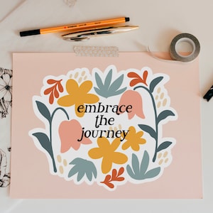 May include: A pink background with a white sticker featuring a floral design and the text "embrace the journey".