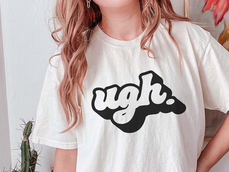 May include: A white t-shirt with a black graphic that says "ugh" in a retro, bubble-letter style.