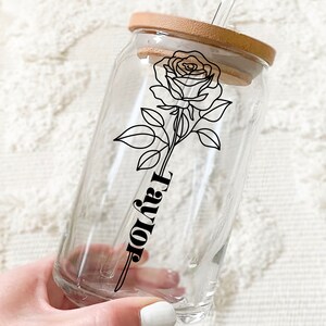 May include: A clear glass reusable drinking cup with a wooden lid and a black and white line drawing of a rose and the word "Taylor".