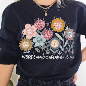 May include: A navy blue sweatshirt with a floral design and the text "WORDS matter SPEAK kindness". The flowers are filled with positive messages like "you are loved", "the world needs you", "you deserve joy", "let's focus on the good", "hard times you'll grow the most", "take a deep breath", "I'm here for you", and "you're very strong".