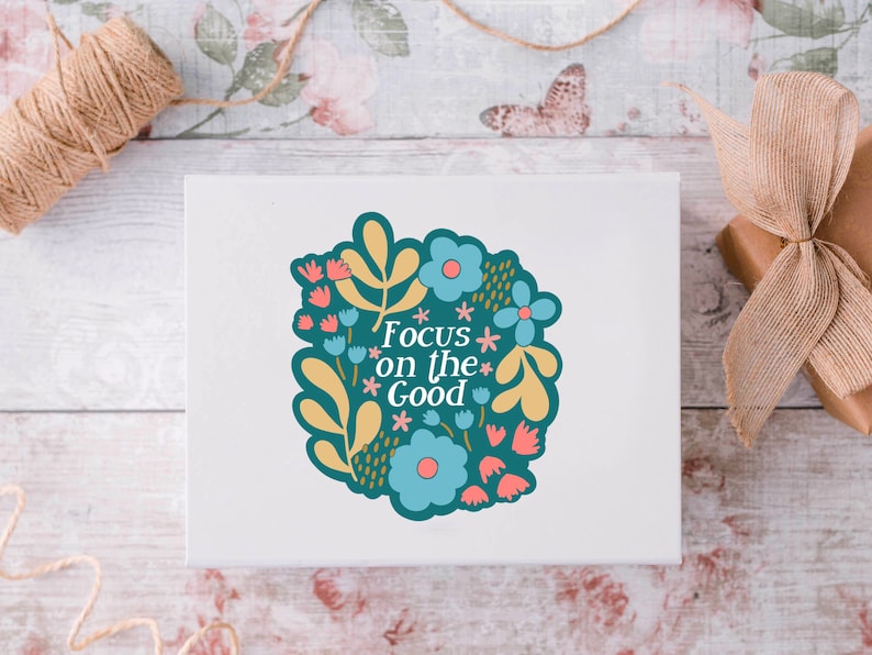 May include: A white card with a teal blue floral design and the text "Focus on the Good" in white.
