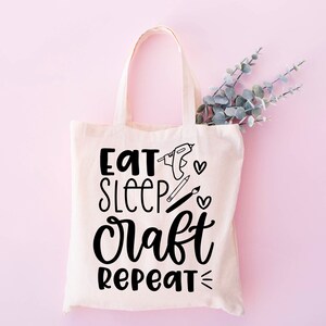 May include: A white canvas tote bag with black text that reads "Eat Sleep Craft Repeat" and includes illustrations of crafting tools.