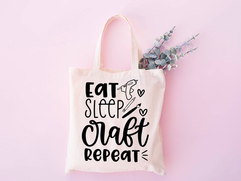 May include: A white canvas tote bag with black text that reads "Eat Sleep Craft Repeat" and includes illustrations of crafting tools.