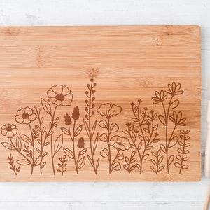 May include: A brown bamboo cutting board with a floral design engraved on the bottom edge. The design features a row of stylized flowers and leaves.