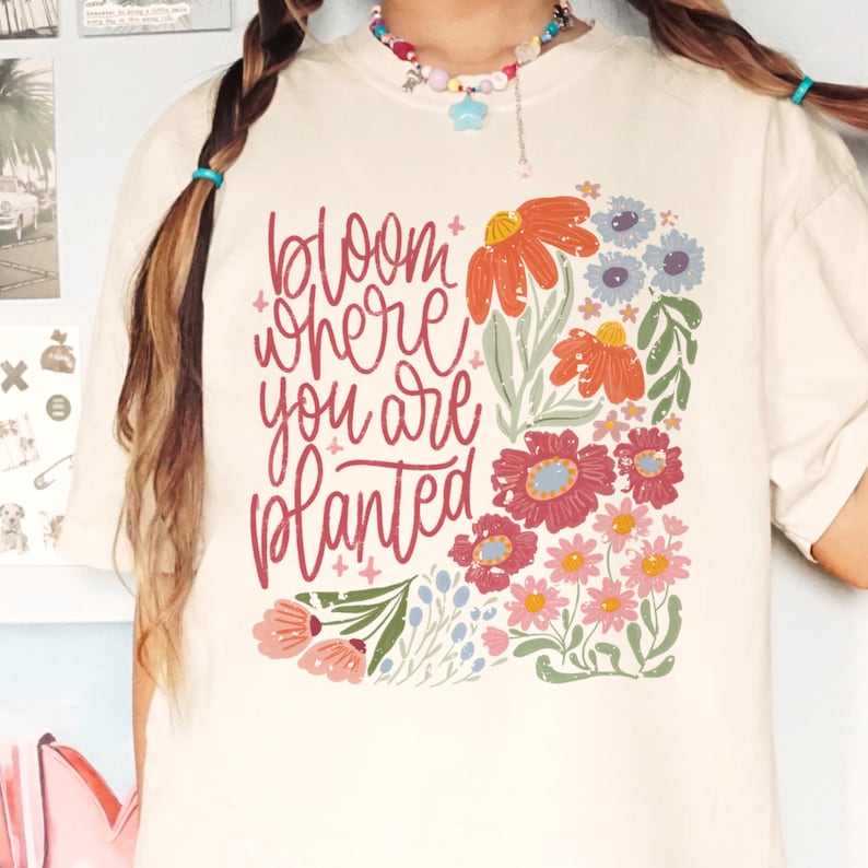 May include: A white t-shirt with a floral design and the text "bloom where you are planted" in red.