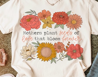 May include: A white t-shirt with a floral design and the text "Mothers plant seeds of love that bloom forever".