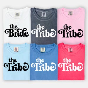 May include: Six t-shirts in different colors with the text "the Bride" and "the Tribe" in a retro font. The shirts are all the same style and size.