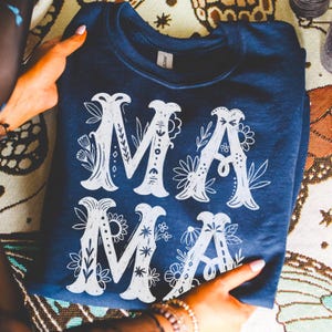 May include: A navy blue sweatshirt with a white floral design that spells out "MAMA".