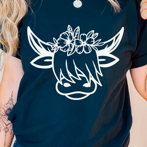 May include: Black t-shirt with a white outline of a Highland cow wearing a flower crown.