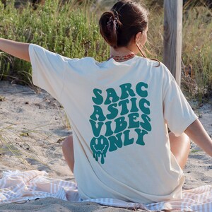 May include: A white t-shirt with a green graphic that says "SARCASTIC VIBES ONLY" with a dripping smiley face.