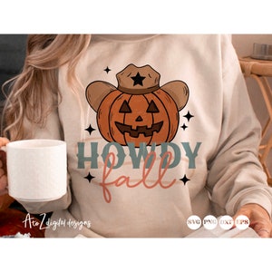 May include: A beige sweatshirt with a graphic design of a pumpkin wearing a cowboy hat. The text "Howdy Fall" is written in a stylized font below the pumpkin.