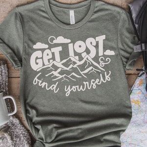 May include: A green t-shirt with white text that reads "Get Lost & find yourself". The text is surrounded by a graphic of mountains and clouds.