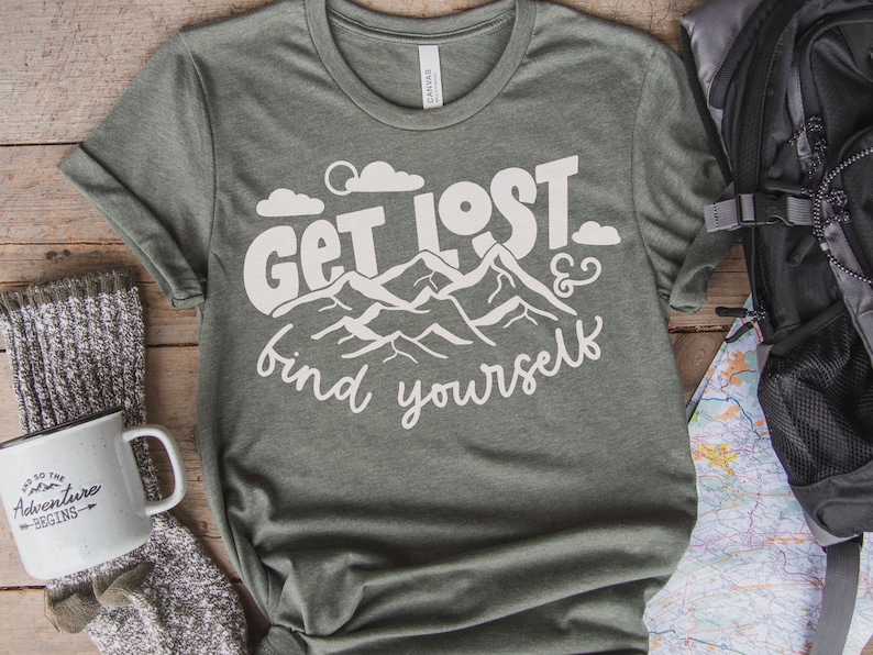 May include: A green t-shirt with white text that reads "Get Lost & find yourself". The text is surrounded by a graphic of mountains and clouds.