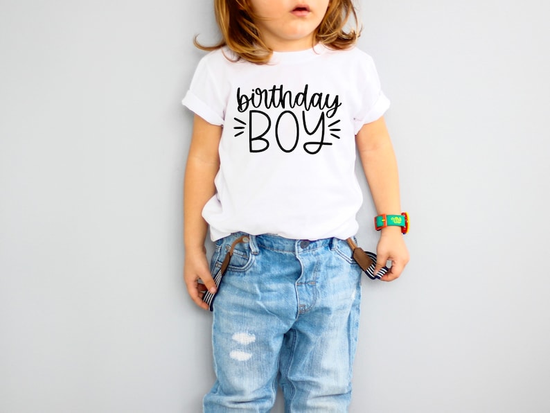 Op de afbeelding: Een wit T-shirt met zwarte tekst die "birthday boy" zegt met een stervormig ontwerp aan beide kanten van het woord "boy".