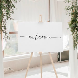 May include: A white sign with the word "welcome" written in black cursive script on an easel.
