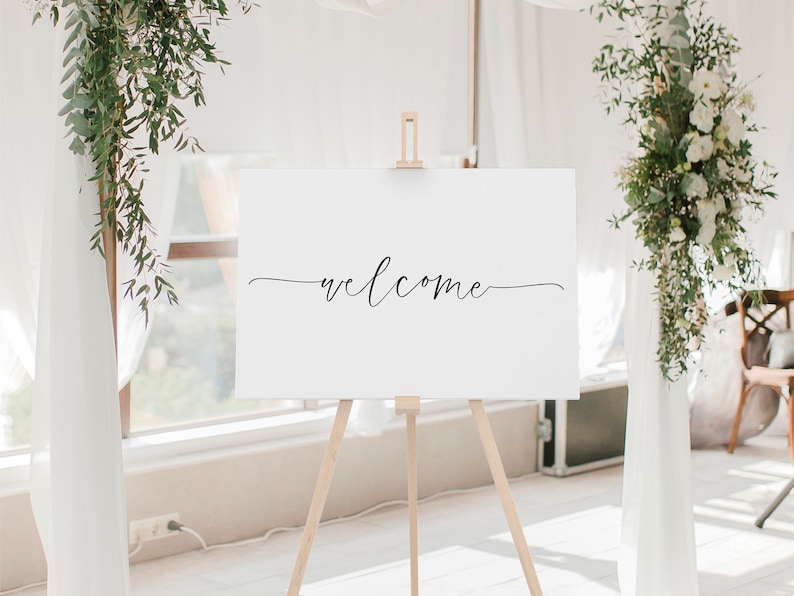 May include: A white sign with the word "welcome" written in black cursive script on an easel.