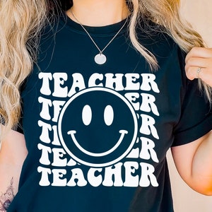 May include: Black t-shirt with a white smiley face and the word "TEACHER" repeated in a retro font.