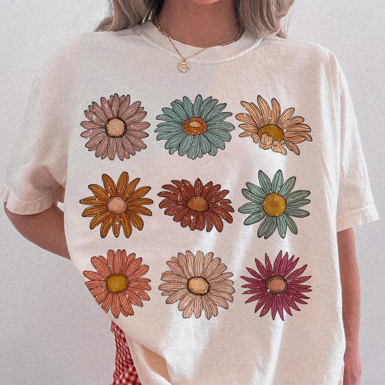 May include: White t-shirt with a floral print featuring nine colorful daisies in a grid pattern.