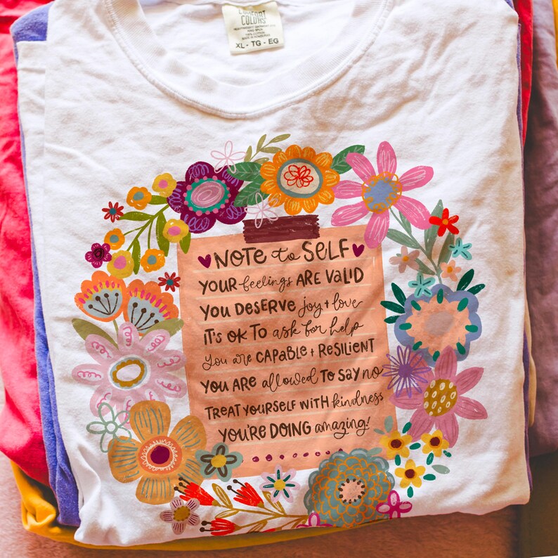 May include: White t-shirt with a floral design surrounding a note that reads "Note to Self." The note includes positive affirmations such as "Your feelings are valid" and "You're doing amazing!"