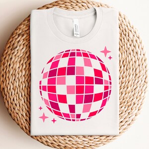 Pu&ograve; includere: Maglietta bianca con una grafica di palla da discoteca rosa e rossa e due piccole stelle rosa.