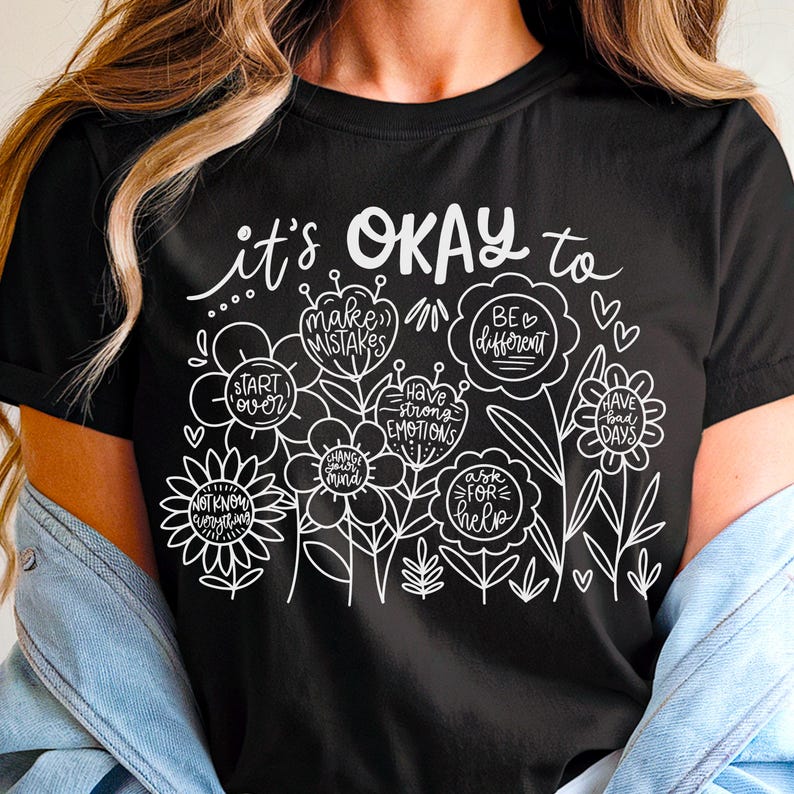 May include: Black t-shirt with white text that reads "it's OKAY to" and features a floral design with phrases like "make mistakes", "have strong emotions", "be different", and "ask for help".